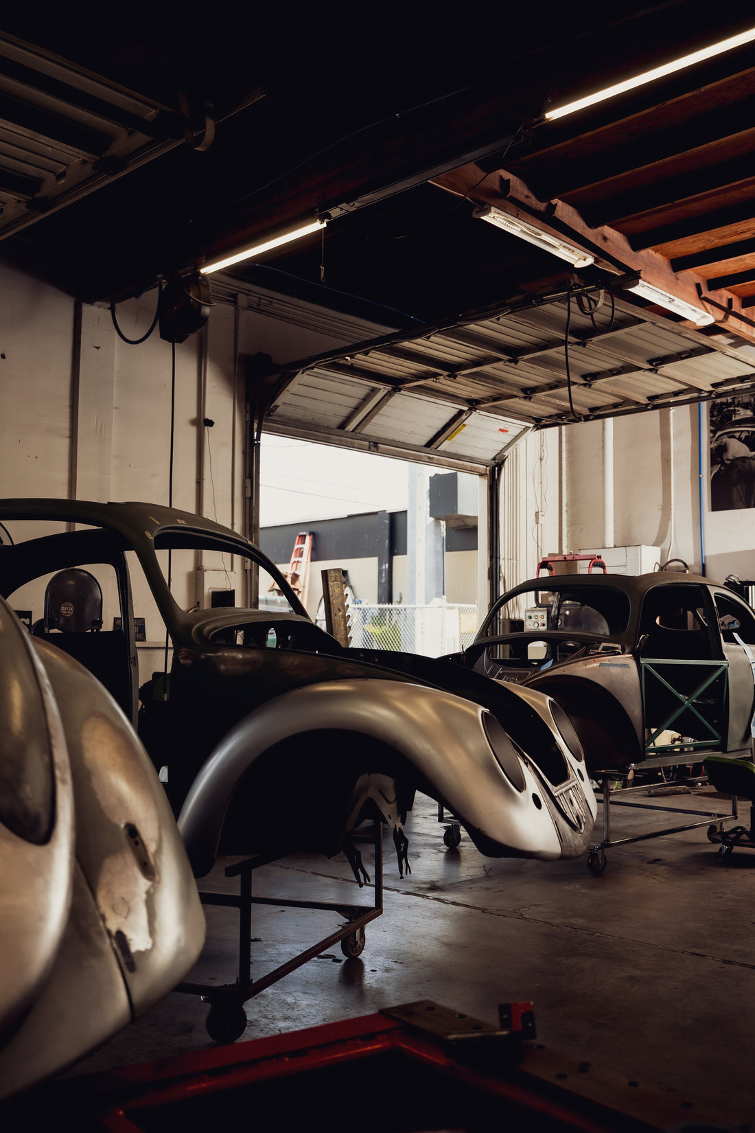 Bare-metal VW Beetle body shells on rolling stands in the Washburn's Metal chassis restoration bay