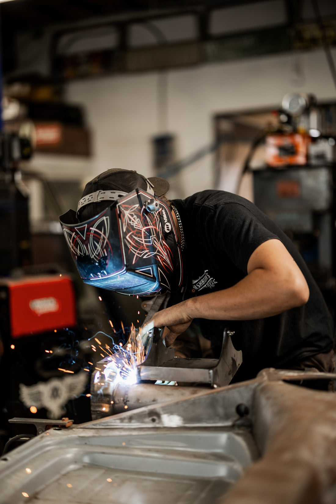 Close-up of a Washburn's Metal fabricator TIG-welding a custom bracket, arc light and sparks visible through the welding helmet