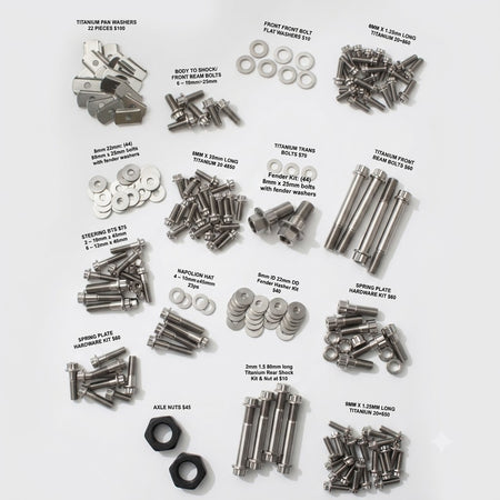An overhead flat-lay of various silver metal automotive hardware components, including bolts, nuts, washers, and pins, arranged on a light gray background with handwritten text labels identifying each part.